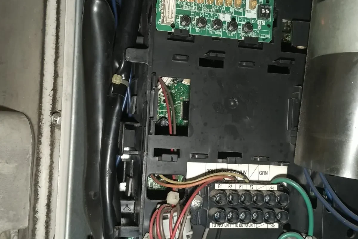 Detailed internal electrical wiring and circuit board of an air conditioner unit undergoing maintenance work.