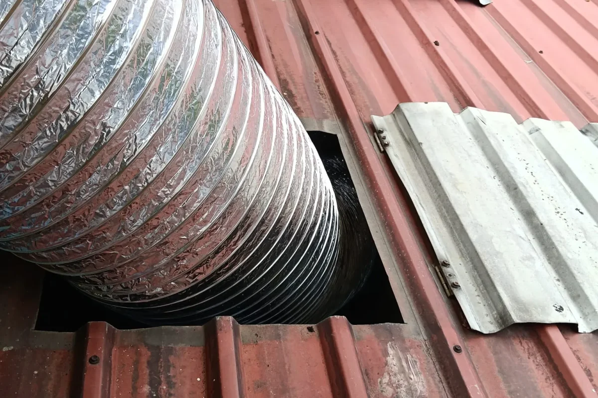 Flexible aluminum air duct pipe installed through a corrugated rooftop opening during ventilation ducting repair work.