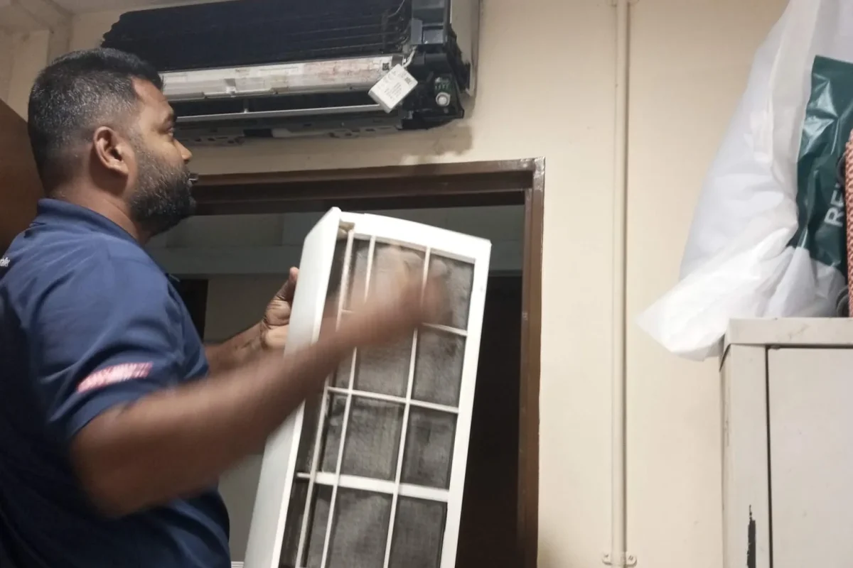 Air conditioner technician holding a front cover and filter during maintenance service.