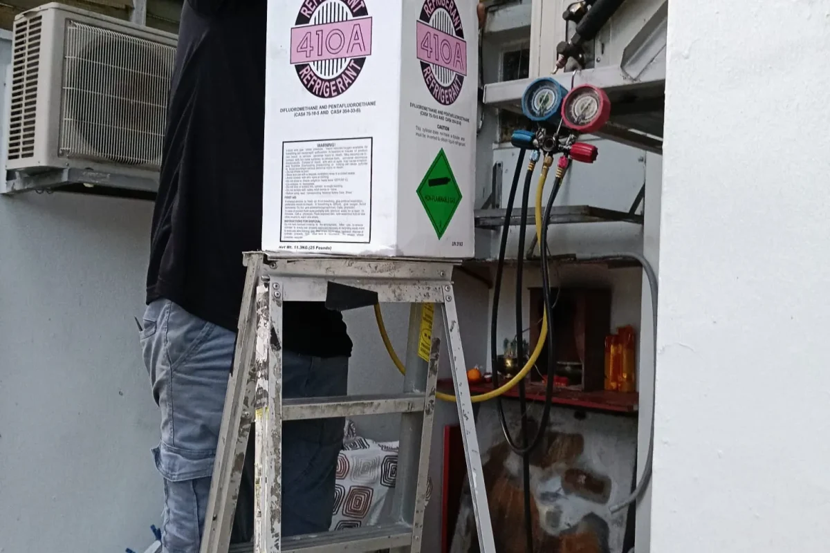 Air conditioner gas top-up and pressure check being performed by a professional technician.